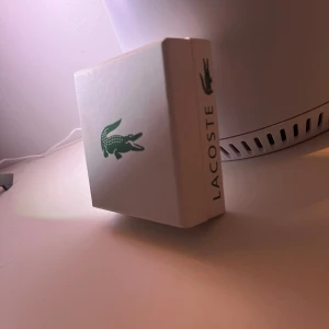 Lacoste silver armband  - Säljer en stilren Lacoste silverarmband  i originalförpackning. Armbandet levereras i en vit box med grönt Lacoste-logga och en vit tygpåse med snörning, också med den klassiska krokodilen. Perfekt accessoar för dig som gillar sportig och clean design.