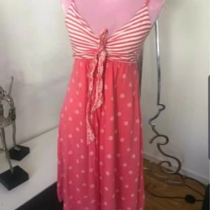 Rosa sommarklänning från Gant - Supersöt rosa kortklänning från Gant med smala axelband. Överdelen har vita och rosa ränder, kjolen är prickig med vita prickar och knytband framtill. Perfekt för varma dagar, lätt och luftig i bomull.