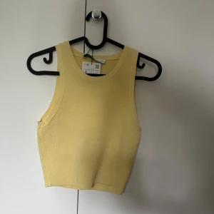Gul croppad linnetopp från Zara - Snygg ljusgul croppad linnetopp från Zara. Toppen är ärmlös med breda axelband och rund halsringning. Perfekt för varma dagar och enkel att styla med jeans eller kjol. Prislappen är kvar. 