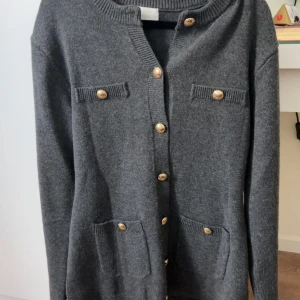 Mörkgrå kofta med guldknappar - Mörkgrå kofta från H&M med snygga guldiga knappar framtill och på fickorna. Långärmad och i mjukt stickat material, perfekt för lager på lager.  Passformen går in vid midjan vilket ger en snatched look och ribbade detaljer vid hals och muddar.