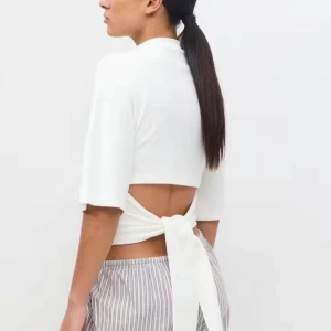 Vit croppad omlottopp med knyt - Säljer en vit croppad topp med halvlånga ärmar och snygg omlottdesign i ryggen som knyts med ett brett band. Toppen har en enkel, stilren look och är tillverkad i mjukt bomullstyg. Perfekt för dig som gillar trendiga och minimalistiska plagg.