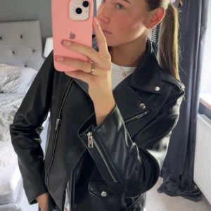 Svart skinnjacka med dragkedjor - Säljer en svart skinnjacka i klassisk bikerstil med silvriga dragkedjor och knappar. Jackan har breda slag, fickor med lock och en cool, tidlös look. Perfekt att slänga över en hoodie eller t-shirt för en edgy vibe. liten i storleken, jag har vanligtvis S