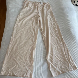 Beiga linnebyxor från H&M, storlek s - Säljer ett par beiga linnebyxor från H&M i storlek s. Byxorna har en avslappnad passform med resår i midjan och raka, vida ben. Perfekta för varma dagar och riktigt sköna att bära. Lätta och luftiga i materialet.