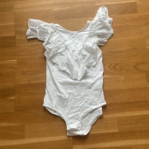 Vit volangbody från Zara - Supersöt vit body från Zara med stora volangärmar i broderad spets och rund halsringning. Perfekt för dig som gillar romantiska detaljer och vill sticka ut lite extra. Knäppning i grenen för enkel användning. Passar dig som vill ha en feminin och trendig look.