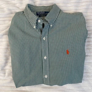 Grön rutig skjorta Polo Ralph Lauren - Snygg grön och vit rutig skjorta från Polo Ralph Lauren i slim fit-modell. Klassisk button-down krage och broderad orange logga på bröstet. Perfekt för dig som gillar stilrena och tidlösa plagg. Skjortan är i bomull och har knäppning framtill.