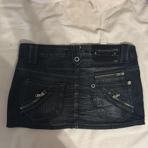 Svart jeanskjol med dragkedjor - kan sänka pris vid snabb affär😉Cool svart jeanskjol i kort modell med flera silvriga dragkedjor och detaljerade fickor både fram och bak. Kjolen har dubbla knappar framtill och markerade sömmar som ger en edgy vibe. Perfekt för dig som gillar streetstyle och vill sticka ut.