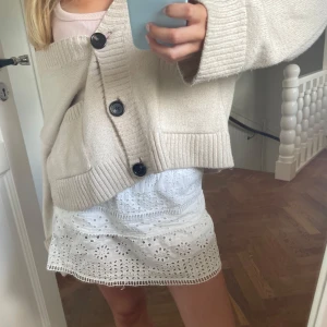 Vit broderad kortkjol i bomull - Supersöt vit kortkjol med broderade blommor och hålmönster. Kjolen har resår i midjan och volangig nederkant, perfekt för sommarens alla tillfällen. Lätt och luftig i bomull, ger en fräsch och romantisk vibe.