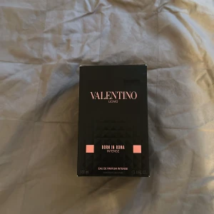 Valentino Uomo Born In Roma Intense 100ml - Valentino Uomo Born In Roma Intense är en lyxig herrparfym i en svart, nitat glasflaska med rosa detaljer. Flaskan rymmer 100 ml och har en cool, edgy design med tydlig Valentino-logga. Doften är en Eau de Parfum Intense och levereras i en matchande svart kartong.