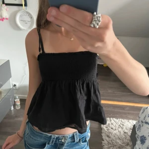 Svart croppad linnetopp - Säljer en svart croppad linnetopp med smockad överdel och tunna axelband. Toppen har en luftig och flowy passform nedtill, perfekt till jeans eller kjol. Enkel och stilren design som är lätt att matcha.