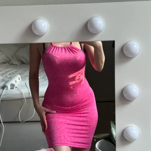 Rosa tight halterneck kortklänning - Supersnygg rosa kortklänning med halterneck och åtsittande passform. Klänningen har ett melerat mönster i olika rosa nyanser och tunna axelband. Perfekt för dig som vill sticka ut och känna dig extra cool.