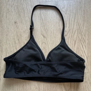 Svart trekantsbikini med justerbara band - En stilren svart trekantsbikini med justerbara axelband. Klassisk modell med bredare band under bysten för extra stöd. Perfekt för stranden eller poolen. Materialet är mjukt och följsamt, vilket gör den bekväm att bära hela dagen.