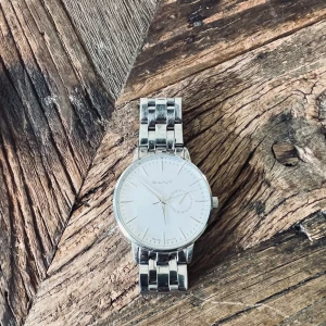 Silverfärgad klocka från Gant modell Park Hill - Stilren klocka från Gant med rund vit urtavla och silverfärgat armband i metall. Klockan har minimalistisk design med diskreta markeringar och en extra liten urtavla för sekunder. Perfekt accessoar för en clean look. Behöver dessvärre nytt batteri. 