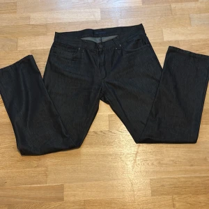 Svarta jeansbyxor från Riley - Snygga svarta jeansbyxor från Riley med klassisk femficksdesign. Byxorna är tillverkade i en mix av bomull och polyester, vilket ger en skön känsla och bra passform. Perfekta för dig som gillar stilrena och enkla svarta jeans.