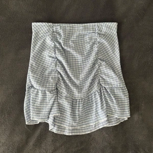 Blåvit rutig volangkjol Gina Tricot - Supersöt blåvit rutig kortkjol från Gina Tricot med volang och rynkade detaljer. Funkar också att använda som en topp! I storlek M, men är stretchig i midjan och passar även S. Helt oanvänd och är därför i väldigt bra skick 💗