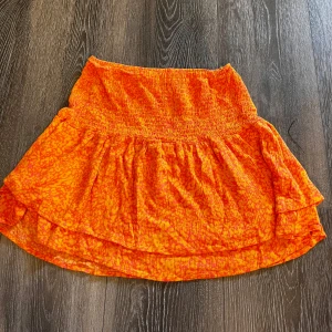 Orange mönstrad kjol från Vero Moda - Superfin kort kjol från Vero Moda i en riktigt somrig orange färg med subtilt mönster. Kjolen har smock i midjan och volangig nederdel.🧡