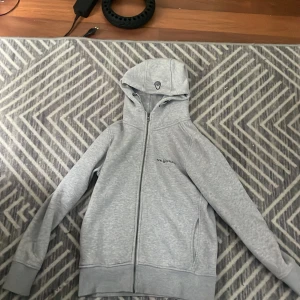 Grå hoodie från Sail Racing med dragkedja - Snygg ljusgrå hoodie från Sail Racing med hel dragkedja och broderad logga på huvan. Tröjan har huva med snörning, två fickor och är tillverkad i mjuk bomullsblandning. Perfekt för chill dagar eller när du vill ha en clean look, storlek S för de som är 150-164cm,PRIS KAN DISKUTERAS.