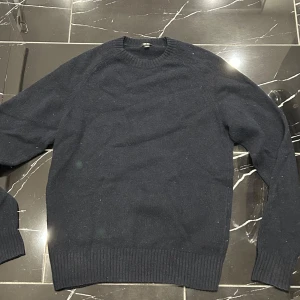 stickad tröja från Uniqlo - En enkel och stilren mörkblå stickad tröja från Uniqlo. Tröjan har rund halsringning, ribbade muddar och är långärmad. Perfekt för lager-på-lager och passar till det mesta. Materialet är ull som är mjukt och skönt, vilket gör den riktigt bekväm. Inga defekter 