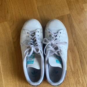 Vita adidas stan smith  - Klassiska Adidas Stan Smith sneakers i vitt skinn med snörning och rund tå. Hälpartiet har en blåskimrande detalj med Stan Smith-logga och ormskinnsmönster. Perfekta för en clean och sportig look. I använt skick därav priset. Kontakta gärna för mer bilder eller frågor!🥰
