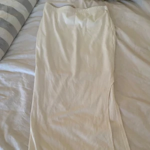 Vit ribbad långkjol med slits - Säljer en stilren vit långkjol med ribbad struktur och en snygg slits på sidan. Kjolen har en rak och tight passform och är perfekt för dig som gillar minimalistisk stil. Superenkel att matcha med olika toppar! 