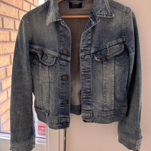 Klassisk blå jeansjacka från Lee - Snygg blå slim jeansjacka från Lee. Jackan har bröstfickor med knappar, krage och långa ärmar. Perfekt för dig som vill ha en tidlös och avslappnad look.