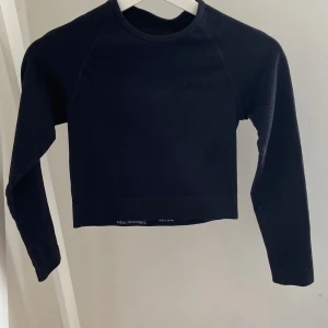 Svart croppad tränings tröja från new apparel  - Svart croppad långärmad träningströja. Tröjan är ribbad och har en enkel, stilren design med rund halsringning. Perfekt för dig som gillar en clean och sportig look.