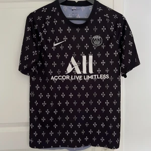Svart PSG fotbollströja Nike - Svart PSG fotbollströja från Nike med vitt tryck och små siffror över hela tröjan. 