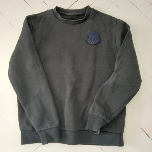 Svart sweatshirt från Moncler - En stilren svart sweatshirt från Moncler med rund hals och diskret broderad logotyp på bröstet. Tröjan har långa ärmar, ribbade muddar och är tillverkad i mjuk bomull. Perfekt för dig som gillar en clean och klassisk look. Hör av dig om du vill ha mer bilder eller information😁