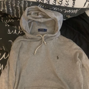 Grå hoodie från Polo Ralph Lauren - Snygg grå hoodie från Polo Ralph Lauren med klassisk broderad logga på bröstet. Tröjan har huva med dragsko och är tillverkad i mjuk bomull. Perfekt för en chill och stilren look. Skick 10/10