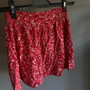 Röd blommig kortkjol från new yorker  - Supersöt röd kortkjol från new yorker i storlek XS med blommigt mönster och smockad midja. Kjolen har en flowy passform och är perfekt för dig som gillar färg och mönster. Lätt och luftig, passar perfekt till varma dagar.