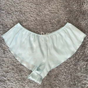 Ljusblå satinshorts från Primark - Superfina ljusblå satinshorts från Primark med pärlrosett i midjan. De har en flowy passform och diskret blommönster i tyget. Perfekta för sommarkvällar eller som mysiga pyjamasshorts. Aldrig använd, endast testad! Står strl M men står Eur 40/42 så L! Jag skulle säga att dom passar L och M! 