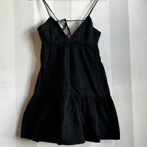 Svart kort klänning/top  från Zara - Supersöt svart klänning/top  från Zara med tunna axelband och v-ringning. Modellen är kort med volang nertill och har en luftig passform. Perfekt för varma dagar eller när du vill känna dig extra chill. Materialet känns lätt och bekvämt.