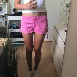 Rosa shorts med knyt i sidorna💓 - SuperSnygga rosa shorts med low/midwaist passform och knytband i sidorna för extra detalj. De har fickor både fram och bak samt bälteshällor. Perfekta för sommaren och riktigt sköna att bära till allt. De har förnuvarande ingen knapp men funkar bra med nål annars💓