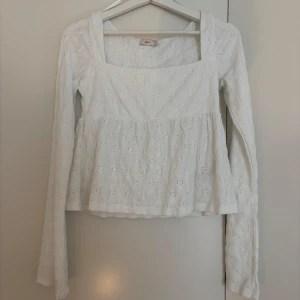 Vit blus med broderade detaljer Nelly - Supersöt vit blus från Nelly med broderade blommönster och fyrkantig ringning. Långa ärmar och lätt utsvängd passform nedtill ger en romantisk vibe. Perfekt till jeans eller kjol för en fräsch look. Aldrig använd.