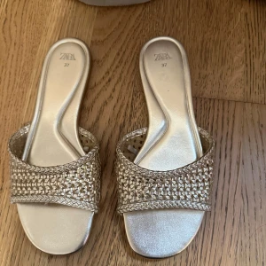 Guldiga sandaler från Zara, flätad rem - Snygga sandaler från Zara i guldig färg med flätad rem över foten och öppen tå. Platt sula och fyrkantig form framtill. Perfekta för sommaren och ger en trendig touch till din outfit.