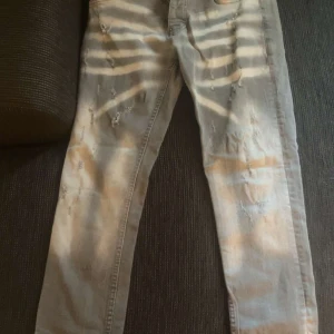 Grå slitna jeans från Dsquared2 - Säljer ett par grå jeans från Dsquared2 med snygga slitningar och distressed detaljer framtill. Jeansen har klassisk femficksmodell, rak passform och är tillverkade i bomull. Perfekta för dig som gillar en cool och avslappnad stil.