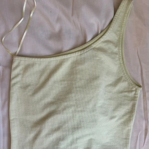 Ljusgul ribbad oneshoulder topp - Trendig ljusgul ribbad topp med oneshoulder-design och smal axelrem. Perfekt för dig som gillar en stilren och modern look. Tunt, mjukt material som känns skönt mot huden och passar till många outfits.