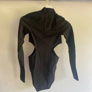 Svart långärmad cut out topp J.Lindeberg - Cool svart långärmad topp från J.Lindeberg med höghalsad design och dragkedja bak. Toppen har unika cut out-detaljer i sidorna som ger en edgy look. Tillverkad i stretchigt syntetmaterial och pryds av J.Lindebergs logga framtill.