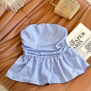 Randig topp  - Supersöt bandeau tubtopp i blått med vita tunna ränder. Toppen har en volangig peplum-nederdel och är axelbandslös, perfekt för en somrig look. Materialet känns lätt och luftigt, vilket gör den extra bekväm.
