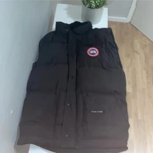 Svart dunväst från Canada Goose freestyle crew - Svart dunväst från Canada Goose med klassisk logga på bröstet och stora fickor framtill. Västen har hög krage och stängs med både dragkedja och knappar. Perfekt för lager-på-lager och riktigt varm under kalla dagar. Köpt på miinto för 7800 kr för 3 mån sen säljer för används ej möts i Stockholm centralt helst kontanter i betalning 