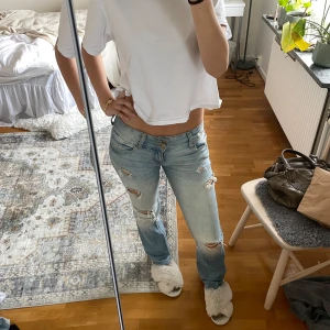 Ljusblå low waist bershka jeans  - Säljer ett par ljusblå jeans med slitningar från bershka som inte sälj längre, har gjort hålen själv. Modellen är lågmidjad med bootcut och klassisk femficksdesign. Jeansen har en avslappnad vibe och är tillverkade i bomull med lite stretch för skön passform. Jeansen har små fläckar på ena bakfickan men det är inget man tänker på