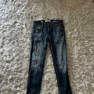 Replay Anbass blå jeans med slitningar - Säljer ett par Replay Anbass jeans i mörkblå tvätt med snygga slitningar och trasiga detaljer på fram- och bakfickor. 