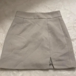 Beige kortkjol med slits - Stilren beige kortkjol med rak passform och liten slits framtill. Perfekt för dig som gillar en clean och enkel look. Kjolen har bred linning och är lätt att matcha med olika toppar.