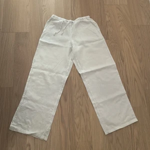 Vita linnebyxor från Gina Tricot - Snygga vita linnebyxor från Gina Tricot med rak passform och dragsko i midjan. Byxorna är tillverkade i ett luftigt linnematerial och har elastisk midja för extra komfort. Perfekta för en chill och stilren look under varmare dagar. Lite genomskinliga 💕