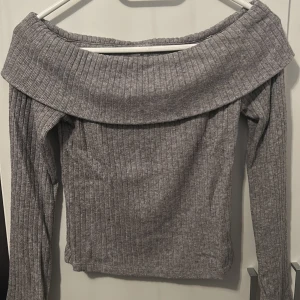 Grå ribbad offshoulder topp Stradivarius - Superfin grå ribbad offshoulder topp från Stradivarius, är lite cropped. Toppen har långa ärmar och bred krage som vilar snyggt över axlarna. Har använts bara ett fåtal gånger. Mjuk och stretchig, perfekt till jeans eller kjol. Säljes i storlek XS💕