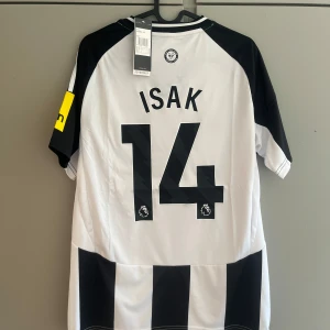 Newcastle United Isak 14 Adidas tröja S - Snygg Newcastle United matchtröja med Isak 14 på ryggen. Klassisk svartvit randig design, broderat klubbmärke, Adidas-logga och sponsortryck. Kortärmad modell i lätt funktionsmaterial, perfekt för fotboll eller att bära på läktaren.