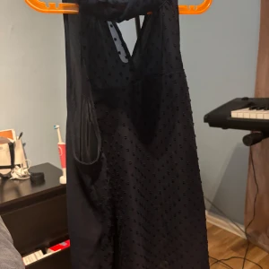 Mörkblå ärmlös blus med struktur - Snygg mörkblå blus med ärmlös design och lätt transparent tyg med små prickar i strukturen. Blusen har en hög hals med knappdetalj i nacken och en liten öppning framtill. Perfekt för dig som gillar stilrena men ändå unika plagg.