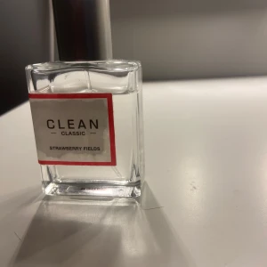 CLEAN Classic Strawberry Fields parfym - Fräsch parfym från CLEAN Classic i doften Strawberry Fields. Flaskan är fyrkantig i genomskinligt glas med en enkel vit etikett och röd ram. Har en stilren silverfärgad spraykork. Perfekt för dig som gillar fruktiga och lätta dofter.