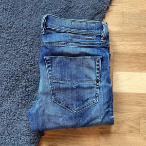 Diesel Tepphar jeans slim fit - Säljer ett par blå Diesel Tepphar jeans med slim-carrot passform. Jeansen har slitningar och hål på låret för en cool, avslappnad look. Klassisk femficksmodell med stretchigt denimtyg och snygga detaljer vid fickorna. Midja 43cm