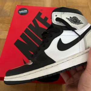 Nike Air Jordan 1 High OG Silver Toe - Nike Air Jordan 1 High OG Silver Toe i svart, vitt och silver. Klassisk high-top siluett med svart swoosh, snörning och perforerad tå. Ovandel i skinn med metallic-detaljer på hälen. Riktigt ikoniska sneakers för dig som vill sticka ut. Använt seriöst 3 gånger. Inget bullshit. Köpte dessa för 2-3 år sedan men inte min stil så använde aldrig dem. De kostar 4 000kr nya så du får en underbar deal