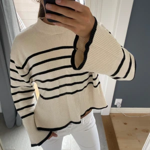 Randig stickad tröja med vida ärmar - Säljer en beige stickad tröja med svarta ränder och vida, långa ärmar. Endast använd någon gång. I storlek XS men skulle mera säga att den passar någon med storlek S